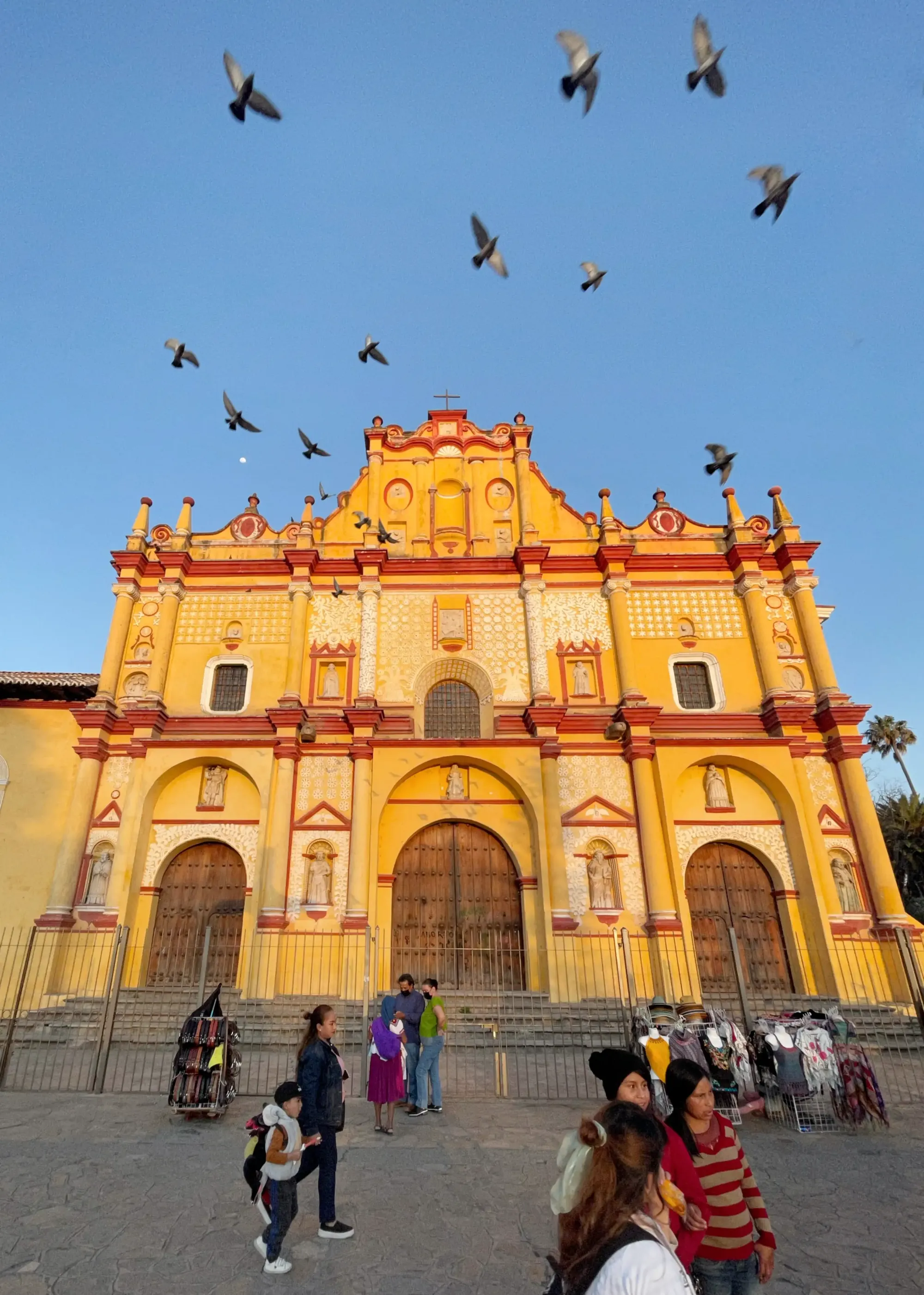 Vendors sell hats outside the Catedral de San Cristóbal Mártir in San Cristóbal de las Casas as a flock of pigeons takes flight overhead.